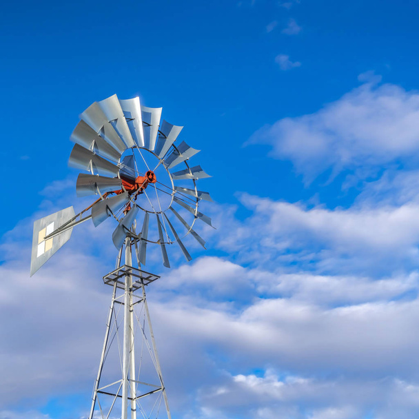 klare quadratische, glänzende Stahlwindpumpe vor einem strahlend blauen Himmel mit Baumwollwolken - Foto, Bild