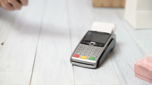 Kobieta płaci za pomocą technologii NFC na karcie bankowej. Terminal płatniczy na białym tle drewnianym. Pudełka upominkowe i terminale do punktów sprzedaży z potwierdzeniem odbioru. Kopiowanie miejsca na tekst - Materiał filmowy, wideo