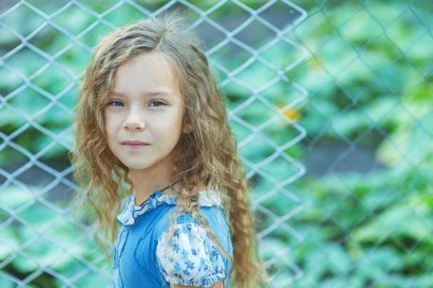 χαμογελώντας μικρό κορίτσι με σγουρά μαλλιά κοντά στο φράχτη του πλέγματος - Φωτογραφία, εικόνα