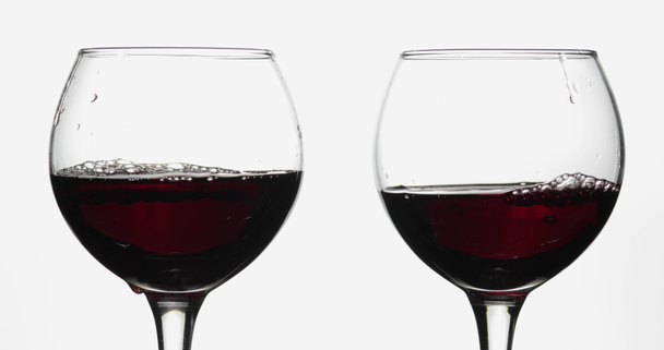 Rose wine. Red wine pour in two wine glasses over white background - Footage, Video