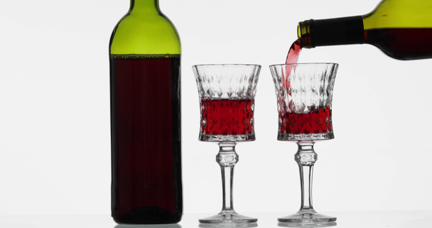 Rose wine. Red wine pour in two wine glasses over white background - Video