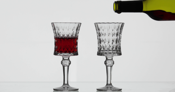 Rose wine. Red wine pour in two wine glasses over white background - Footage, Video