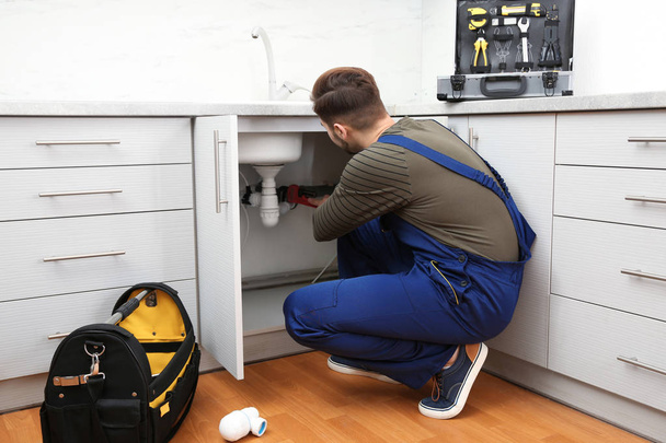 Male plumber in uniform repairing kitchen sink - Φωτογραφία, εικόνα
