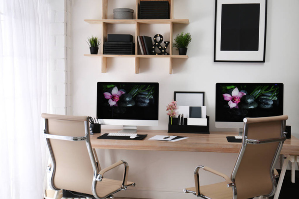 Modern workplace with large desk and computers in room. Stylish interior - 写真・画像