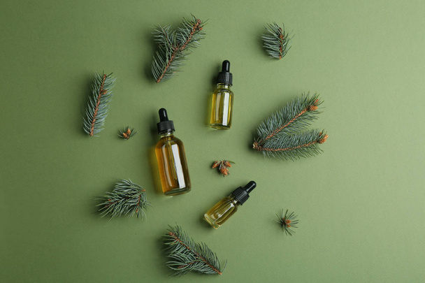 Three little bottles with essential oils and pine branches on color background, flat lay - Foto, afbeelding