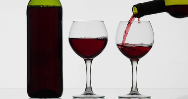 Rose wine. Red wine pour in two wine glasses over white background - Filmati, video