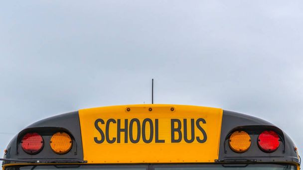Panorama Vista frontale di uno scuolabus giallo con case e cielo nuvoloso sullo sfondo
 - Foto, immagini