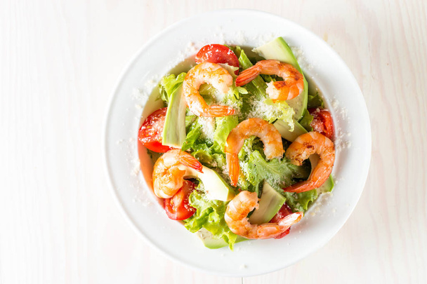 Fresh shrimp salad made of tomato, ruccola, avocado, prawns, chicken breast, arugula, crackers and spices. Caesar salad in a white, transparent bowl on wooden background - Foto, imagen