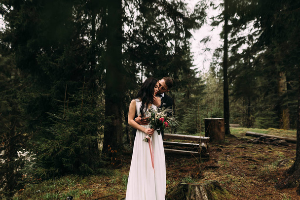 a lovely pair of bride and groom lovers are standing in the forest and smiling - Zdjęcie, obraz
