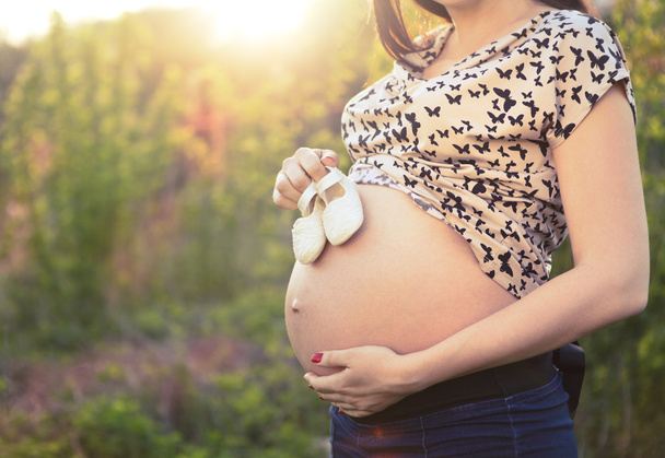 Nahaufnahme einer bis zur Unkenntlichkeit schwangeren Frau mit Babyschuhen - Foto, Bild