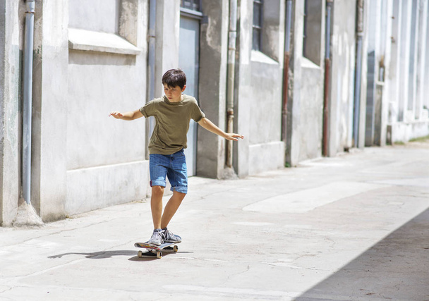 Vista frontal do menino patinador alegre andando na cidade em um dia ensolarado
 - Foto, Imagem