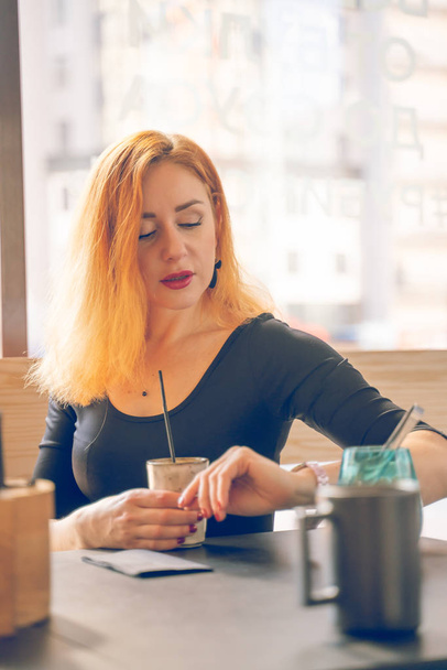 Pretty Happy roodharige blanke vrouw in zwart shirt dranken kopje koffie in het moderne Café alleen - Foto, afbeelding