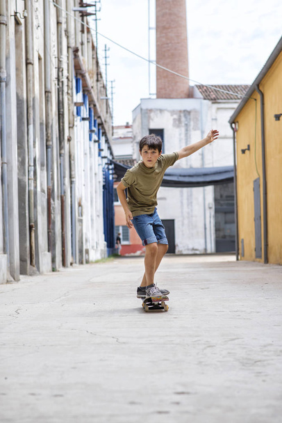 Vista frontal do menino patinador alegre andando na cidade em um dia ensolarado
 - Foto, Imagem