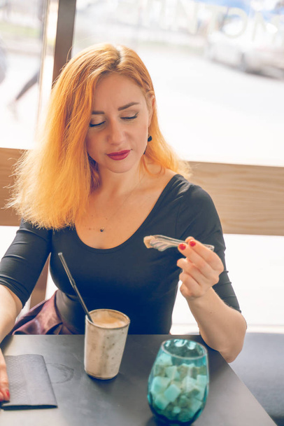pretty happy redheaded caucasian woman in black shirt drinks cup of coffee in the modern cafe alone - Foto, Imagem
