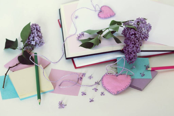 Libros abiertos, marcadores corazones, papel, lápices, ramas de flores lila en la mesa, leer libros románticos y anotar sus pensamientos
 - Foto, imagen