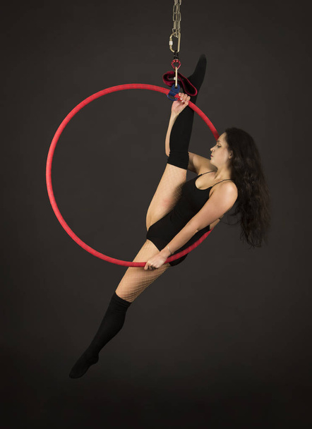 A girl in a dark suit and leggings performs acrobatic elements on the air ring. - 写真・画像