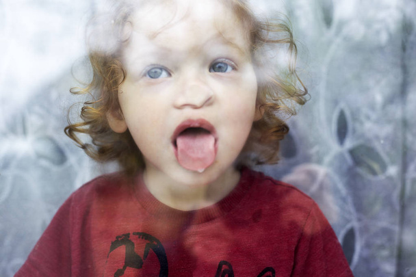 маленька дівчинка показує язик через вікно
 - Фото, зображення