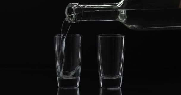 Pouring up two shot of vodka from a bottle into glass. Black background - Footage, Video
