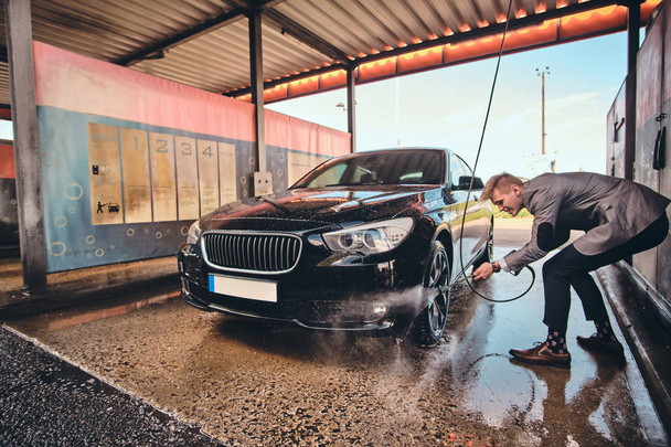Young groomed man is washing his own car at car washing station - Foto, immagini