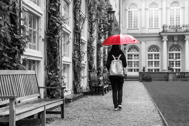 La mujer con el paraguas rojo está caminando en el jardín histórico de un castillo durante el día lluvioso
.  - Foto, Imagen