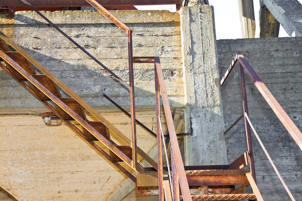 Velha escada de ferro enferrujado contra uma parede de concreto danificado
 - Foto, Imagem