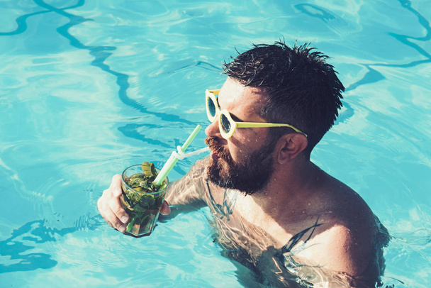 Summer vacation at Miami beach or Maldives. Pool party with hipster in blue water. Cocktail party with bearded man in pool. Relax at sea and spa resort. Man swimming and drink alcoholic mojito - Zdjęcie, obraz
