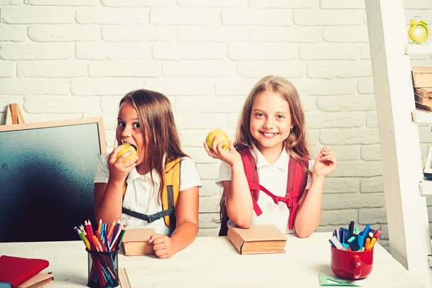 Little girls eat apple at lunch break. Back to school and home schooling. Friendship of small sisters in classroom at knowledge day. School time of girls. Happy school kids at lesson in september 1 - 写真・画像