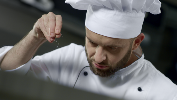 Porträt eines Küchenchefs, der in der Küche Essen salzt. Koch kocht Essen in Zeitlupe - Filmmaterial, Video