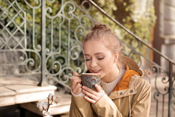 Portrait of young woman enjoying tasty coffee outdoors - 写真・画像