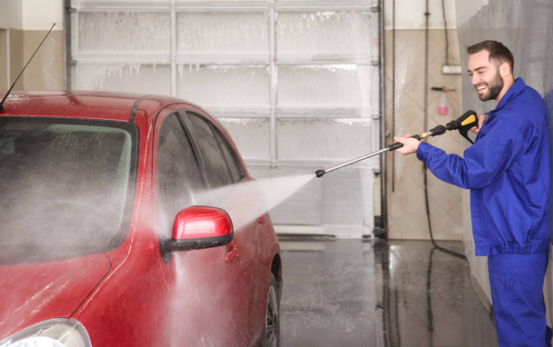 Worker cleaning automobile with high pressure water jet at car wash - Zdjęcie, obraz