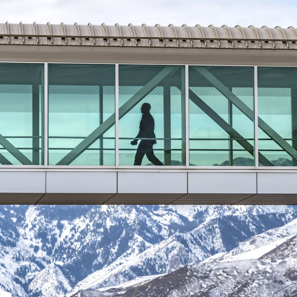 klare quadratische Silhouette eines Mannes, der innerhalb einer Skybridge geht, die Gebäude miteinander verbindet - Foto, Bild