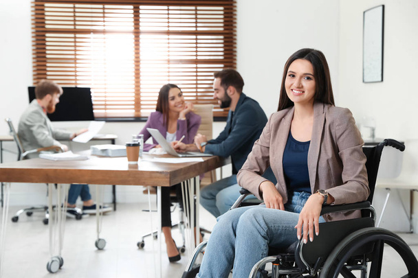 Young woman in wheelchair with colleagues at office - Фото, зображення