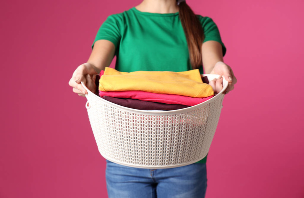 Young woman holding basket with laundry on color background, closeup - Valokuva, kuva