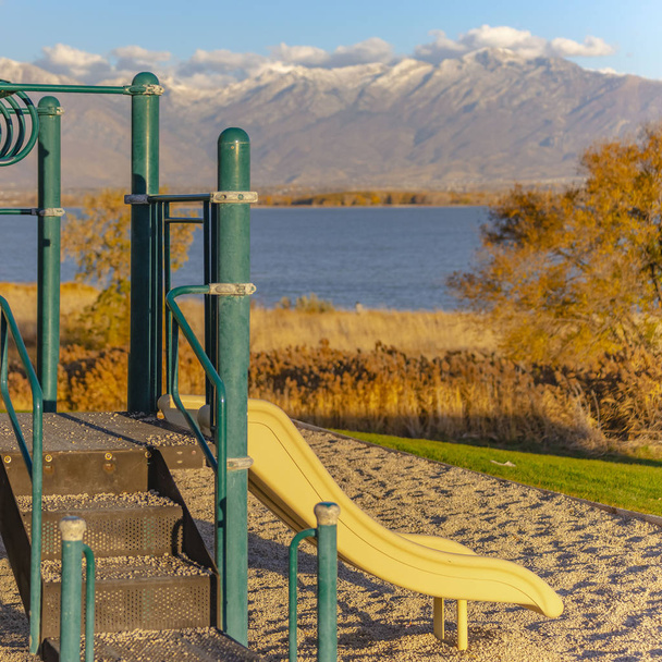 Plaza de diapositivas en un parque infantil con vistas a un lago azul sereno en un día soleado
 - Foto, imagen