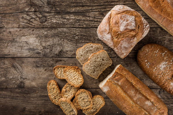 Different fresh bread and spikelets of wheat on rustic wooden ba - Photo, Image