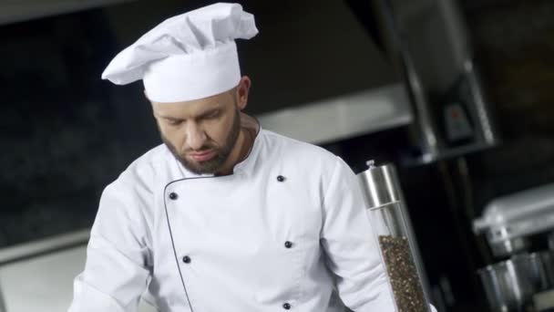 キッチンで食べ物を塩漬けする男性シェフの肖像画。濃縮シェフ料理料理 - 映像、動画