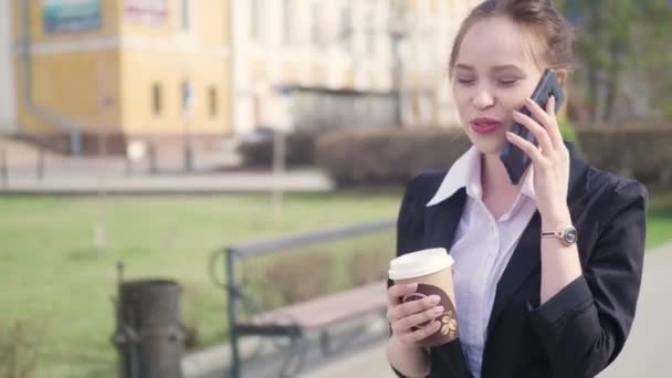 junge erfolgreiche Geschäftsfrau mit Smartphone in der Innenstadt, professionelle Arbeitgeberin im Gespräch mit Geschäftspartnerin beim Kaffeetrinken. Hochhäuser im Geschäftsviertel im Hintergrund - Filmmaterial, Video