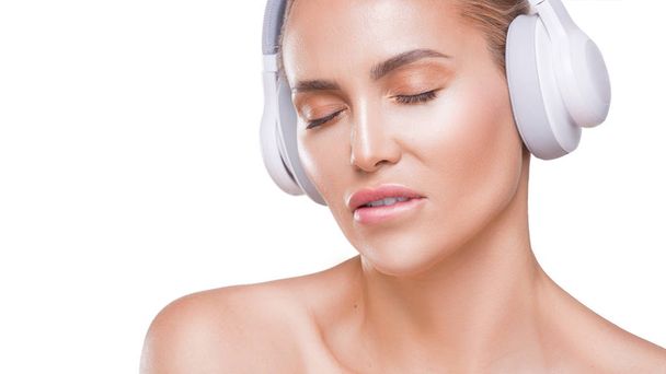 красива жінка в білих навушниках насолоджується музикою, кусає губи, з закритими очима на білому тлі
 - Фото, зображення