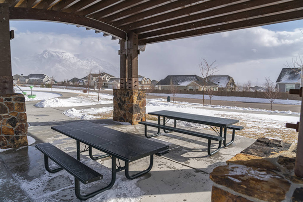 Mesas e bancos dentro de um pavilhão em um parque nevado em um dia ensolarado de inverno
 - Foto, Imagem
