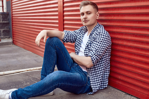 Joven hombre guapo en una camisa y jeans cerca de la puerta roja
 - Foto, imagen