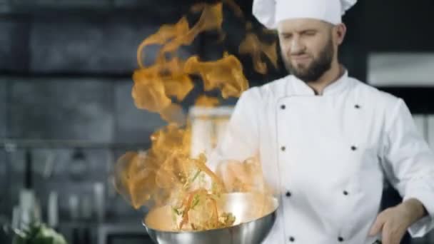 Man chef koken in pan met vuur in slow motion in de keuken. Jonge chef-kok - Video