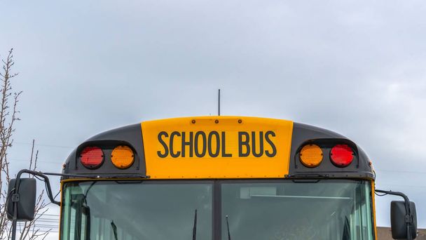 Panorama claro Vista frontal de un autobús escolar amarillo con casas y cielo nublado en el fondo
 - Foto, imagen
