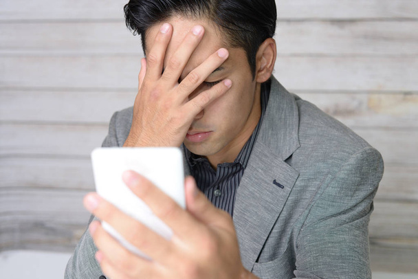 Rozczarowany azjatycki mężczyzna trzyma inteligentny telefon - Zdjęcie, obraz