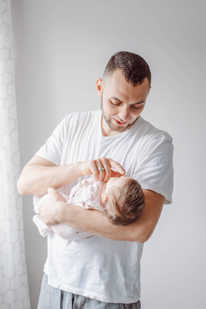 若い白人の父親は新生児を落ち着かせようとしている。男性の親は手にロッキング子を抱いている。本物のライフスタイルドキュメンタリーの瞬間。シングルダッドファミリーライフのコンセプト.  - 写真・画像