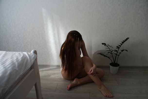 Ένα θλιμμένο κορίτσι με μακριά μαλλιά κάθεται στο πάτωμα.. - Φωτογραφία, εικόνα