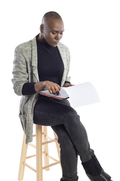 Black African American businesswoman reading contracts or reports or a teacher preparing her lessons for a class or seminar.  She is sitting and isolated on a white background with paperwork. - Foto, Bild