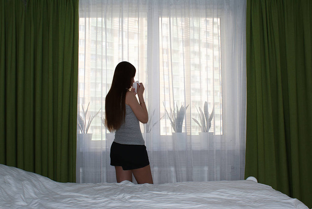 Девушка стоит у окна с чашкой кофе
. - Фото, изображение