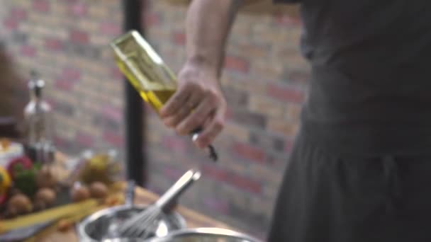 Chef cook pouring olive oil from bottle while cooking salad at bricks background. Male hand taking olive oil bottle while food preparation on kitchen cuisine. Cooking healthy food concept. - Footage, Video