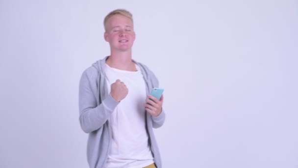Happy young blonde man using phone and getting good news - Video