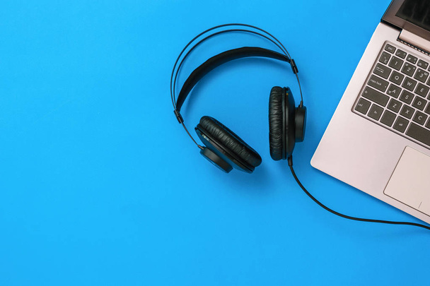 Top view of headphones connected to laptop on blue background. The concept of workplace organization. Flat lay. - Photo, Image